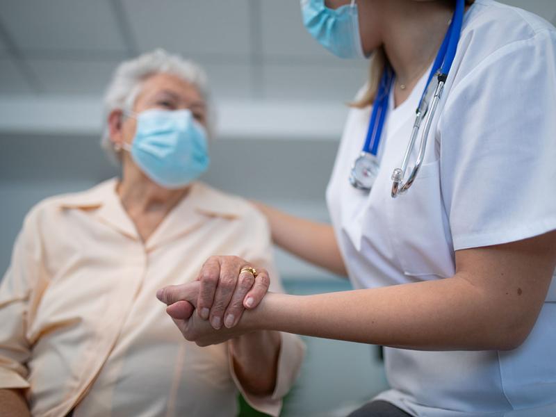 Health care worker holding hands with elderly patient in examination room