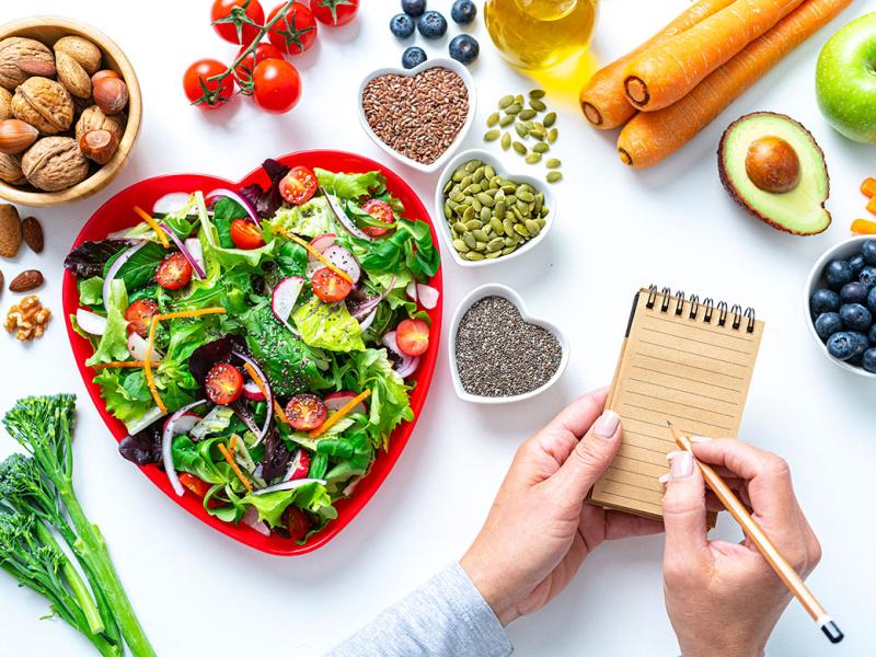 Heart shape plate with healthy salad surrounded by fruit and vegetables
