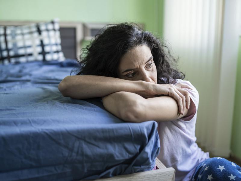 Despondent woman with arms crossed resting head on mattress