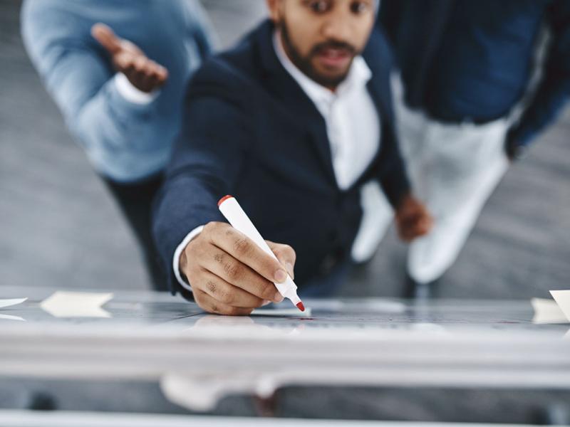 Three businesspeople brainstorming together on a whiteboard in an office