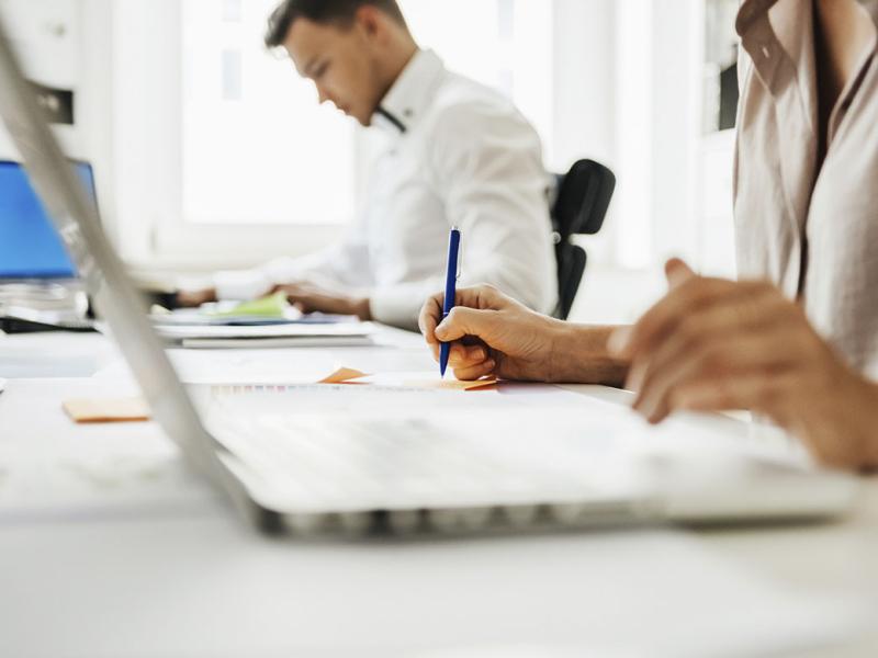 People sitting at a desk and using laptops while working at the office.