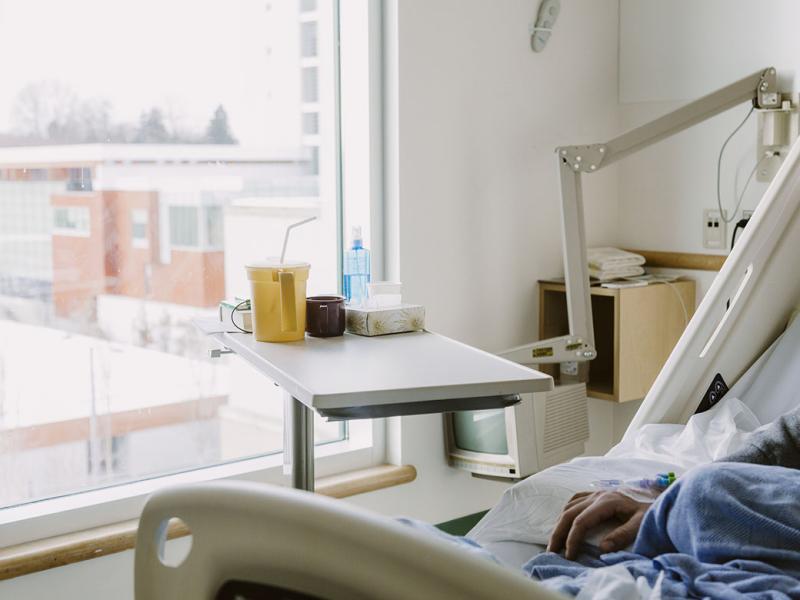 Hand of male sitting in hospital bed looking out the window