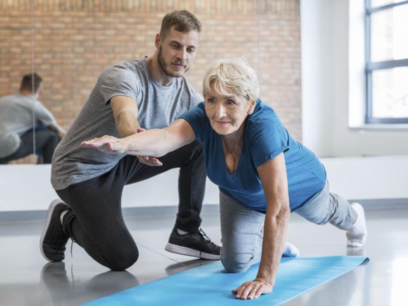 Senior woman being helped by her trainer in doing yoga workout at gym