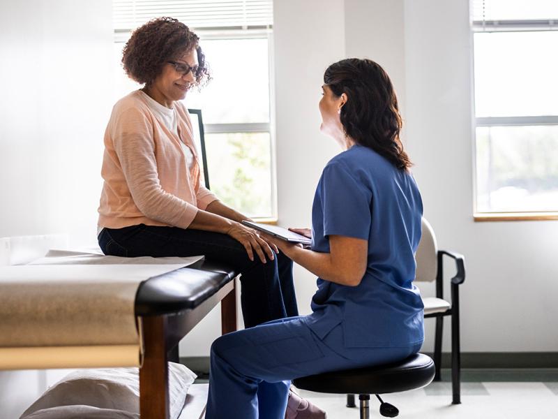 Smiling patient sits on an exam table while talking to health care worker