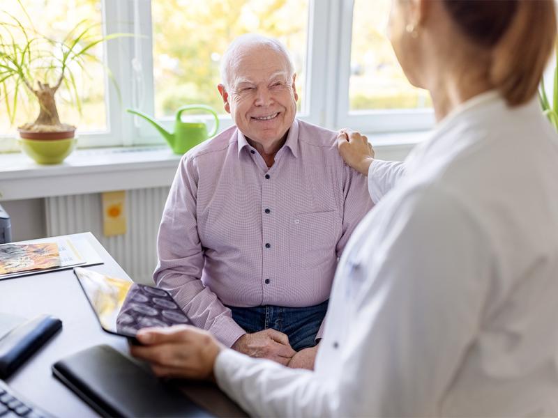 Physician with hand on shoulder of smiling older patient