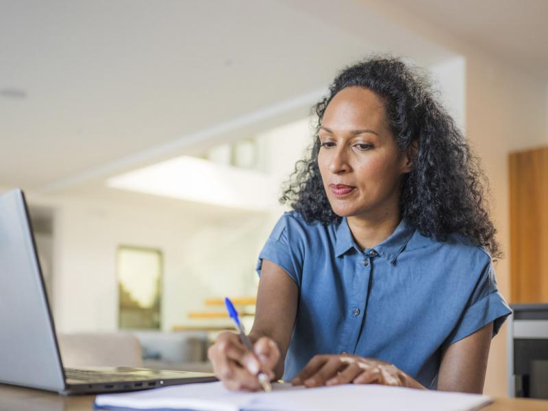 Woman writes while in front of laptop
