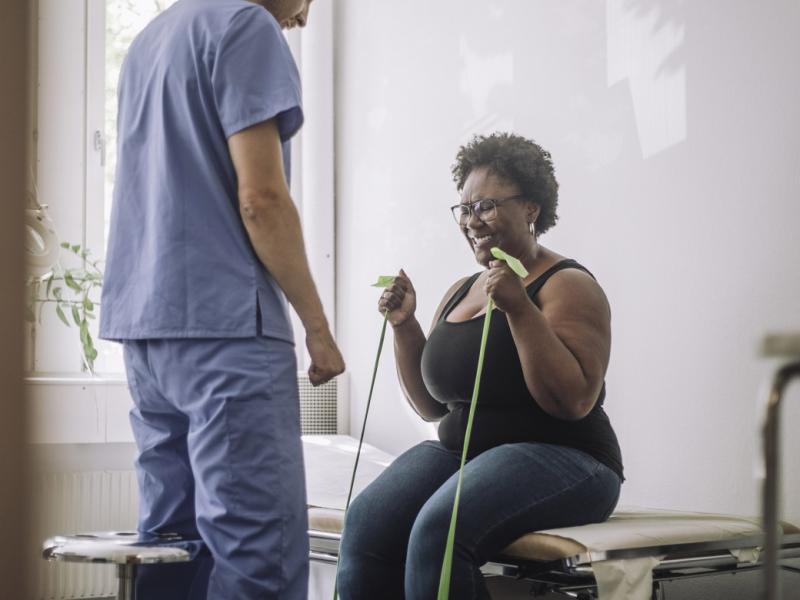 Physical therapist standing by patient exercising with resistance band