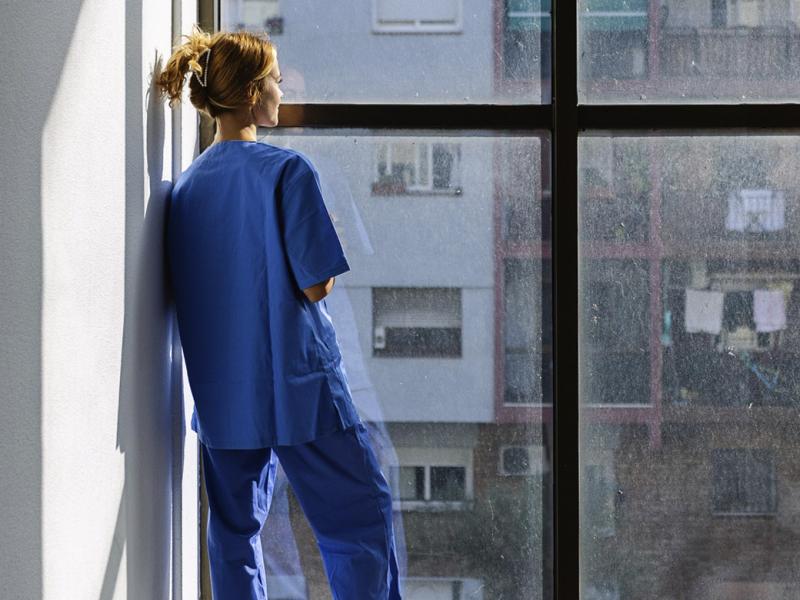 Healthcare worker in scrubs looking out the window
