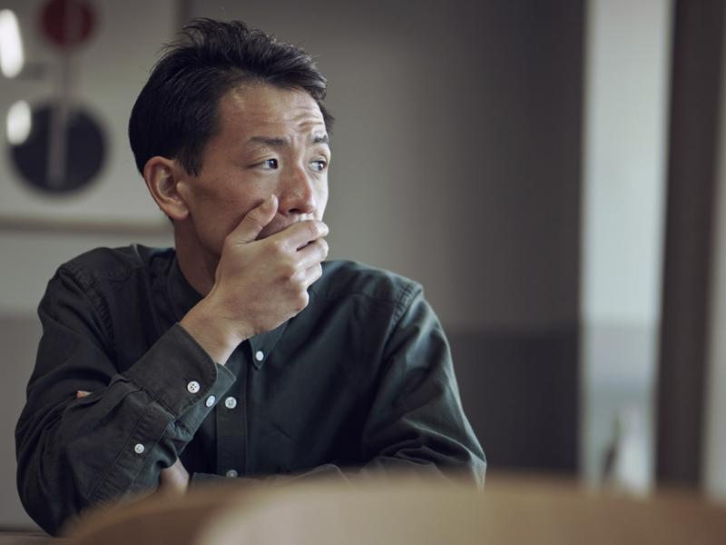 Man sits at table, hand covering mouth