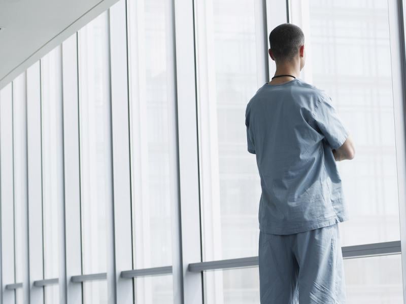Healthcare worker looks out window of hospital corridor