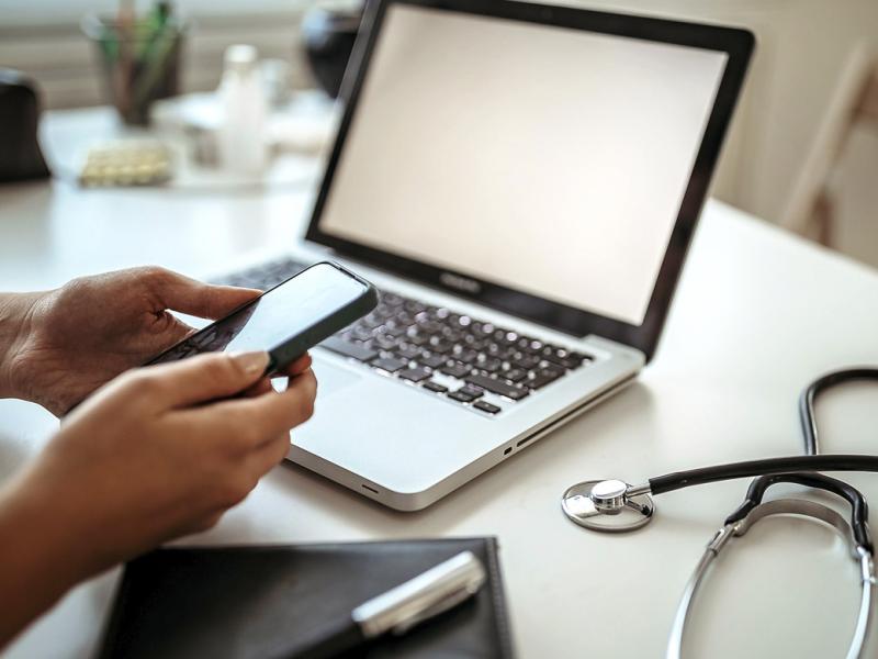 Physician holds a smartphone in front of a laptop