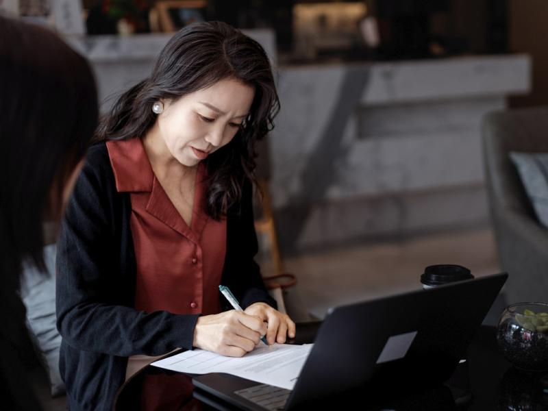 Businessperson signs documents while collaborating with a colleague