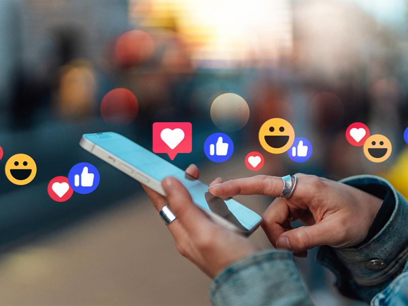 Hand touching smartphone, with likes from social media platform hovering above