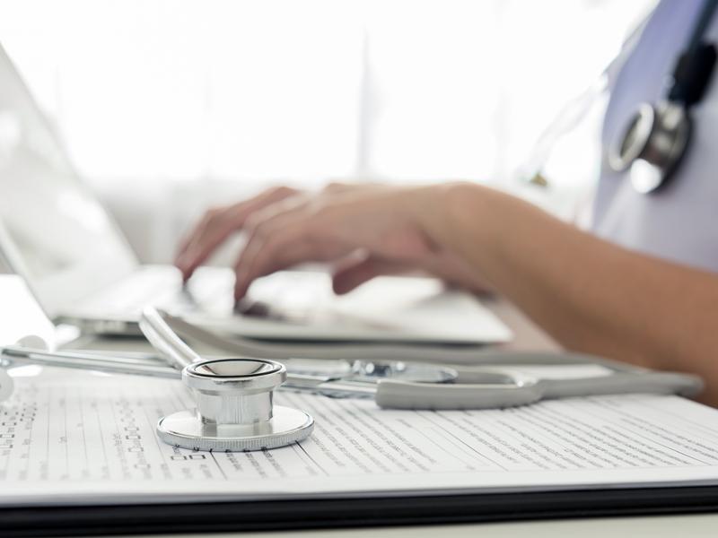 Close up photo of a physician using a laptop with her stethoscope to the side.