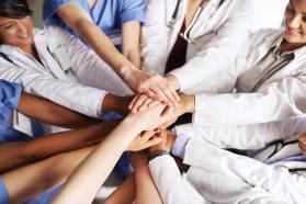 Nine medical professionals putting their hands together in the middle of a group circle