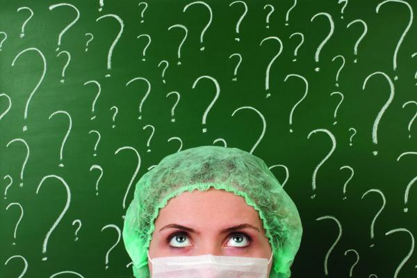 Woman with hair covering and face mask in front of question marks written on a chalkboard