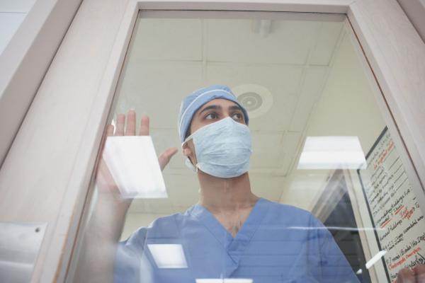 Medical student with mask looking through glass door