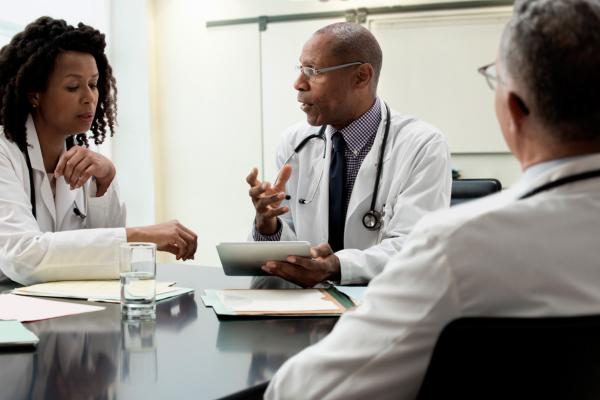 Three diverse physicians meet in a conference room to discuss the medical practice they operate.