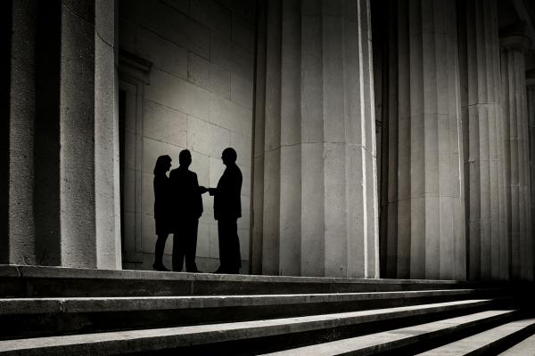 Three people in the shadows of large columns.