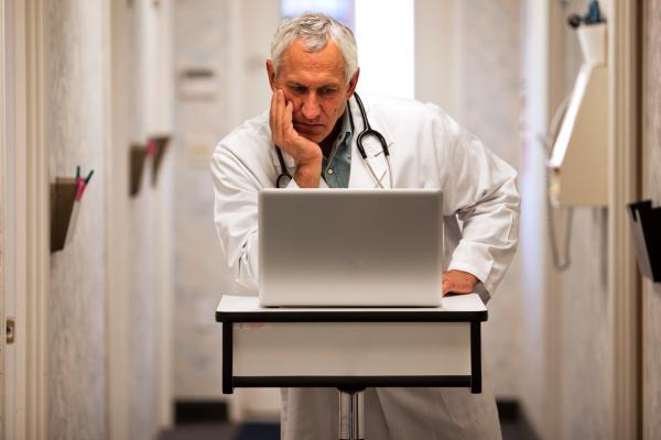 A physician reads a laptop with his hand on his chin.