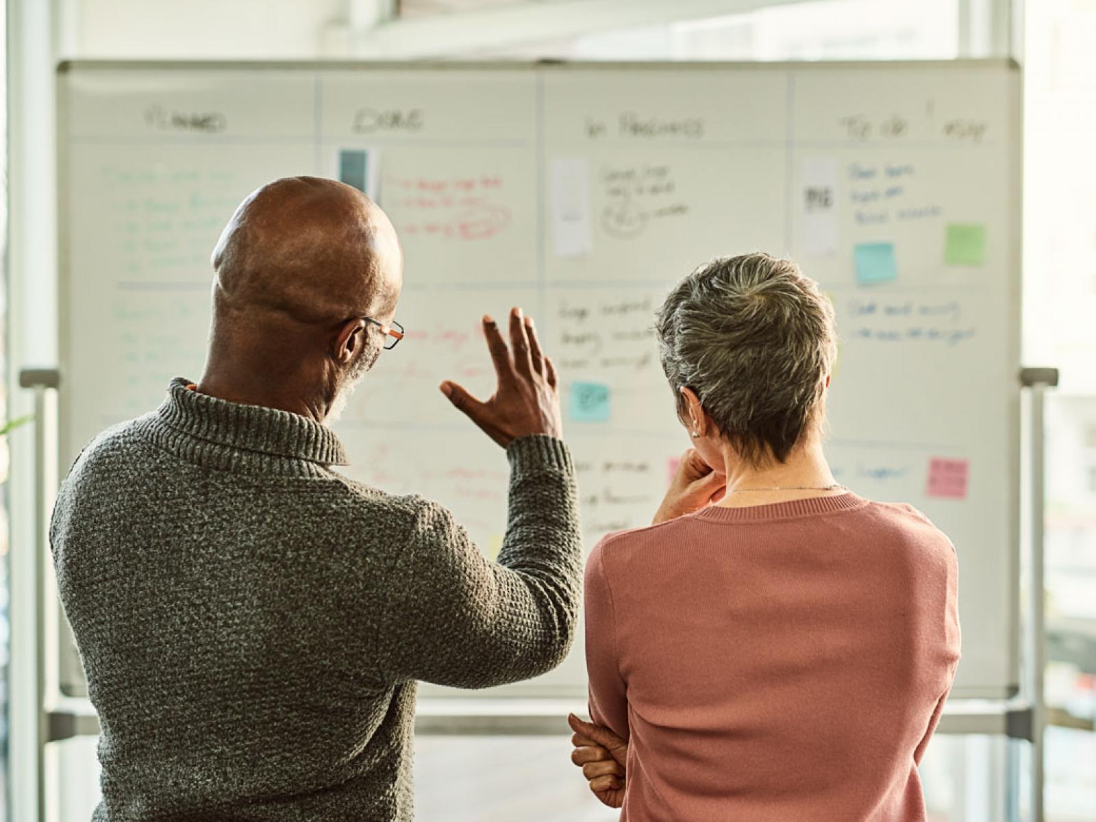 Two people looking at a white board