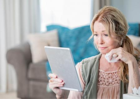 Woman looking at tablet and holding a tissue
