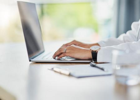 Tight shot of physcian's hands typing on laptop keyboard