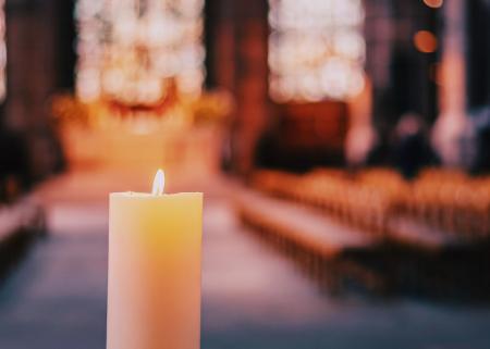 Flickering candle in a church with pews and stained glass windows in background.