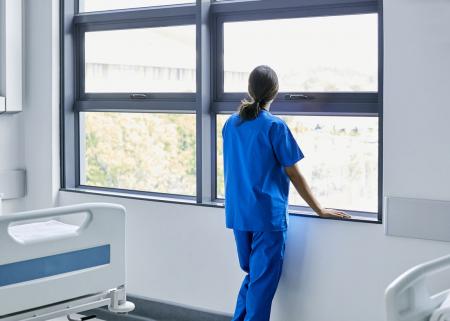 Doctor in scrubs looking out the window of an empty hospital room.