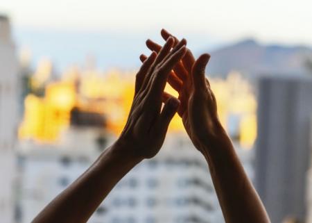 Hands raised in gratitude in front of window