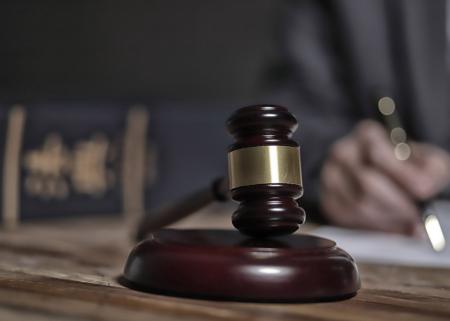 Close-up of a judge's gavel with a blurred out judge writing in the background.