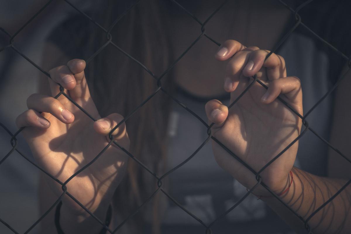 Woman standing behind a fence, holding on