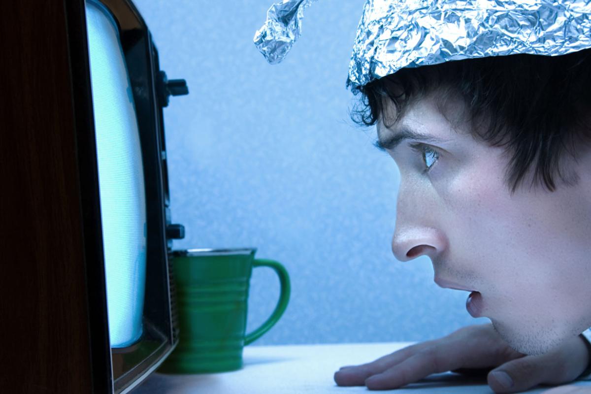 Man in tinfoil hat stares at TV screen