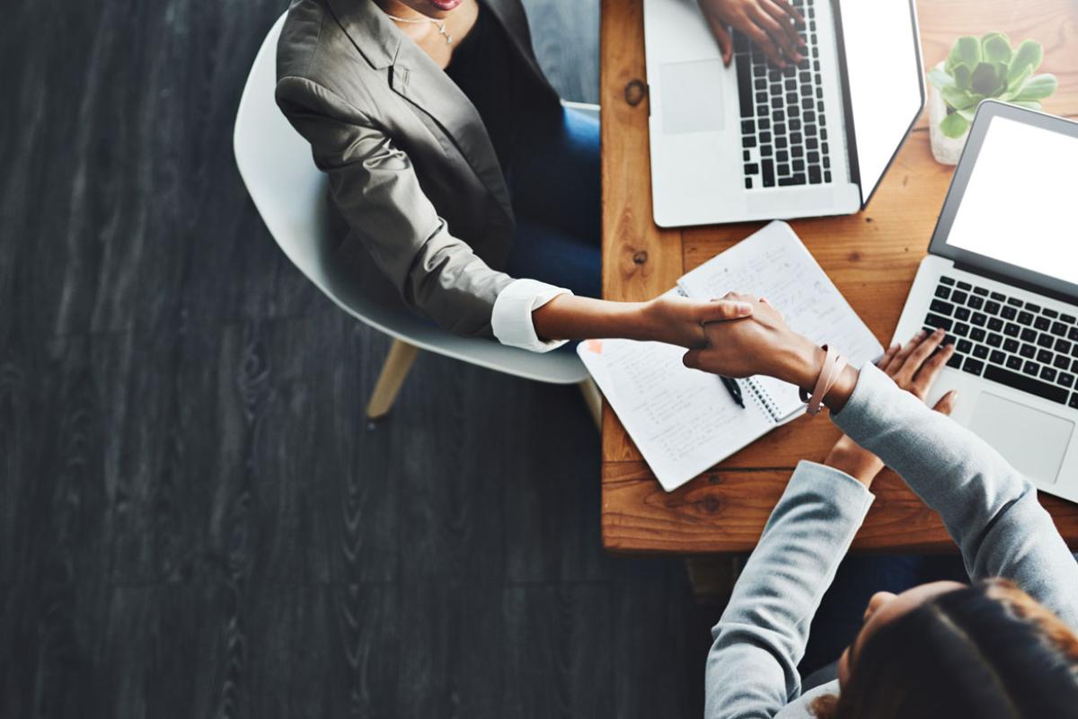 Handshake between two women sitting at a table with laptops