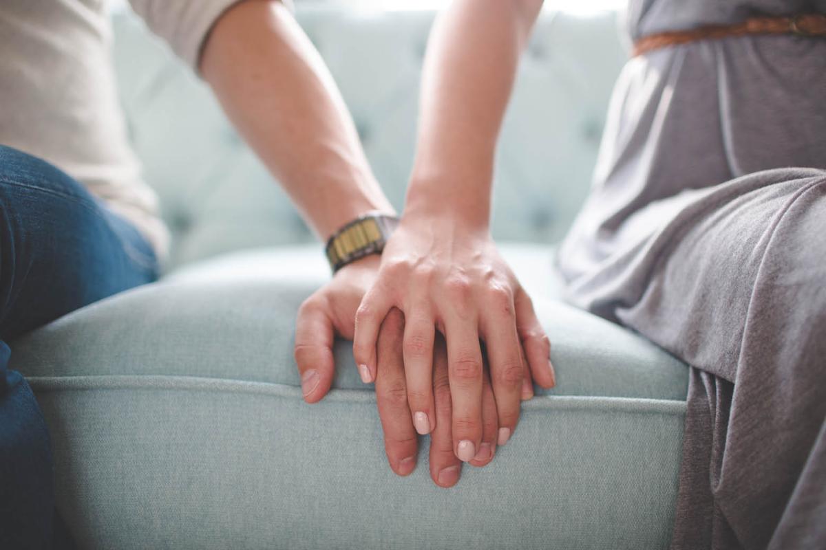 Tight shot of couple sitting on sofa holding hands