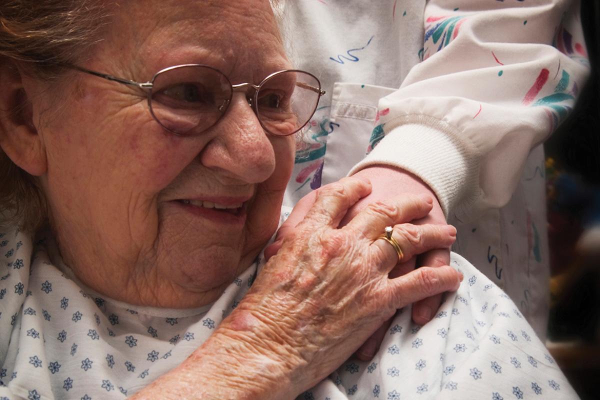 Elderly woman patient smiling and holding hand of caregiver