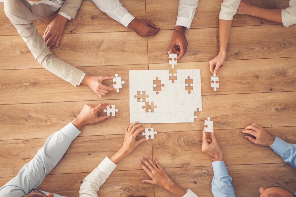 Tight shot of group of people sitting around a table working on a puzzle