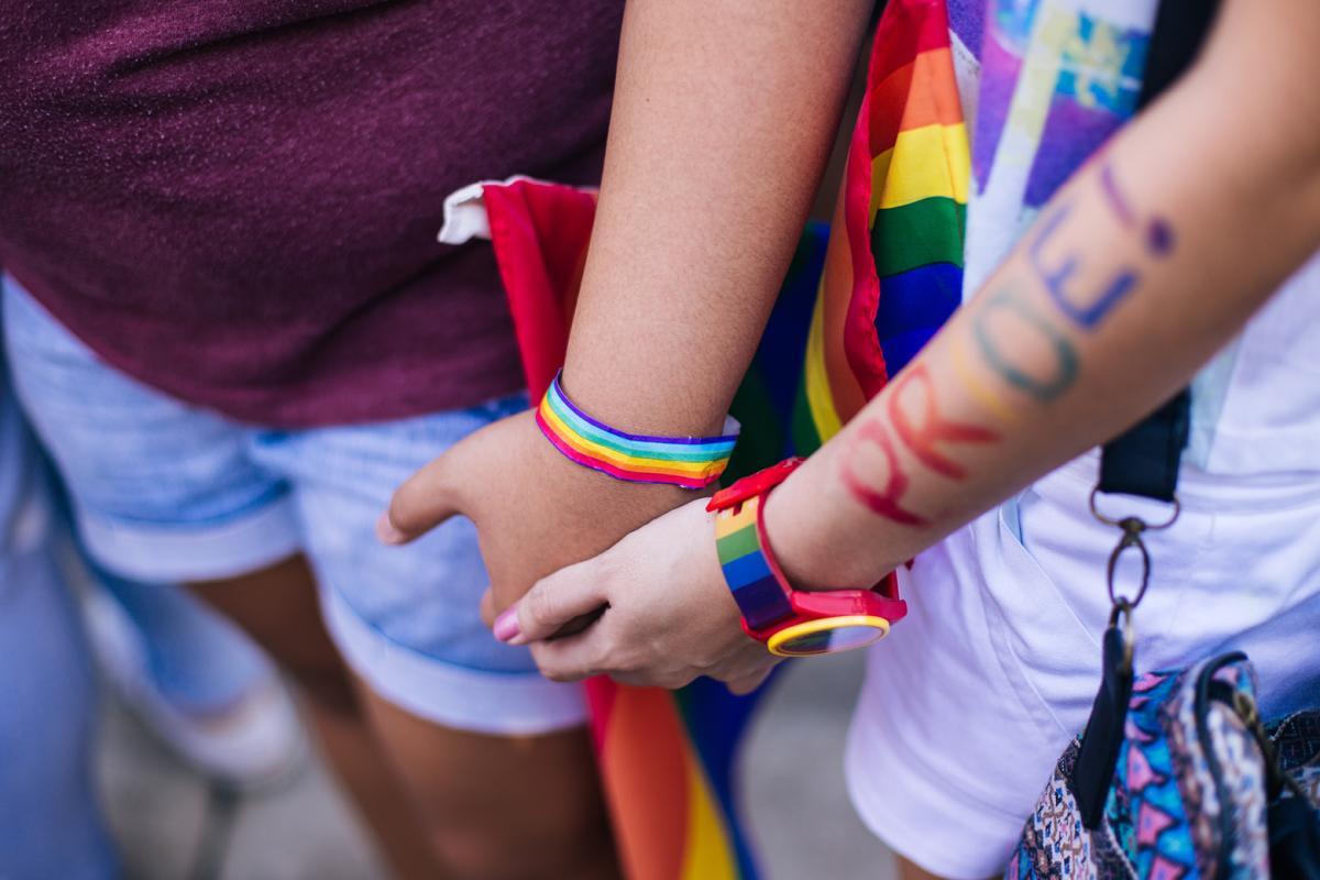 People holding hands with pride bracelets on wrists and"pride" written on arm.