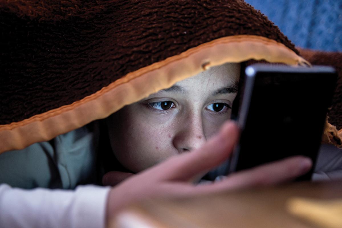 Child looking at mobile phone underneath a blanket