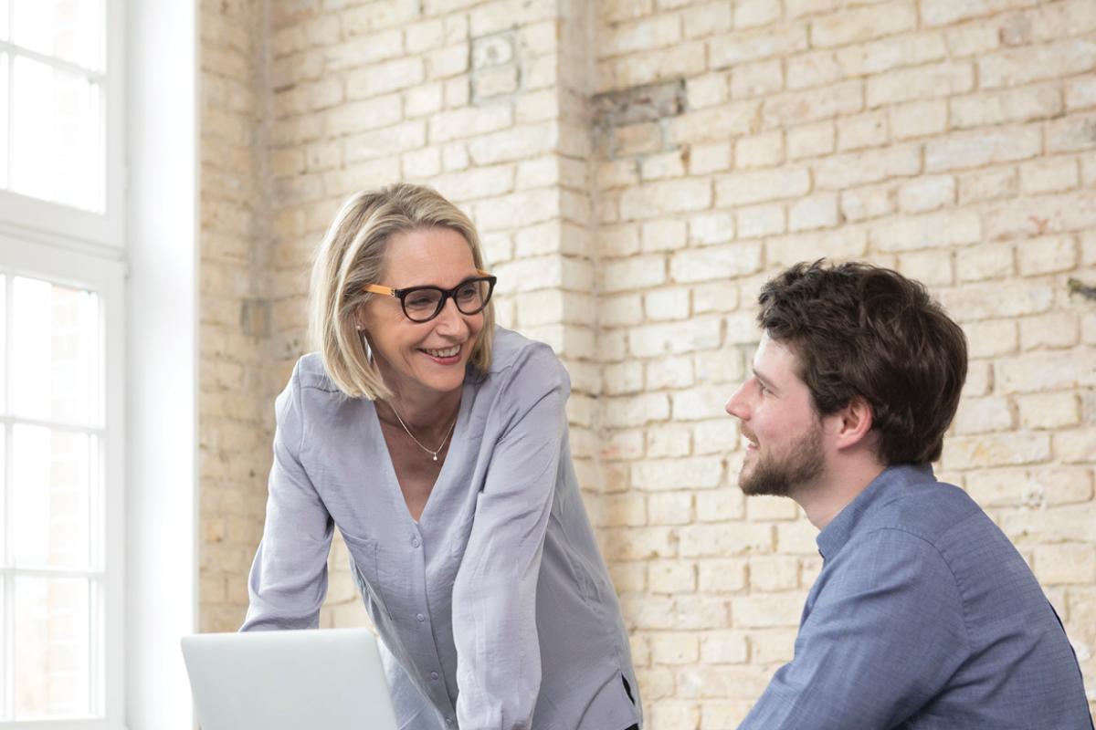 Woman talking with man, standing over a laptop