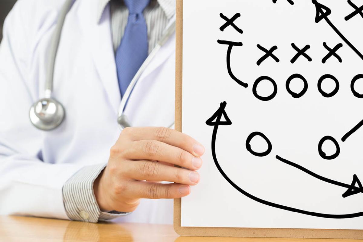 Physician holding a white board with x and o "game plan" drawing