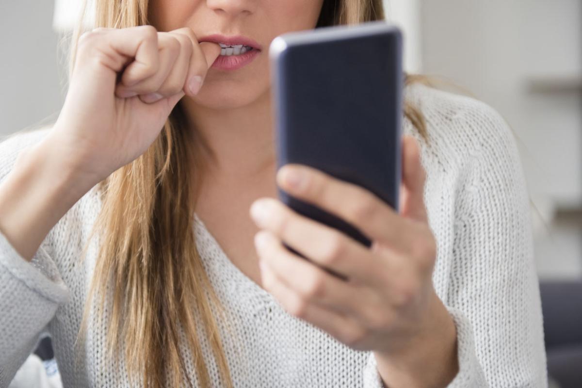 Person biting thumb while looking at smartphone