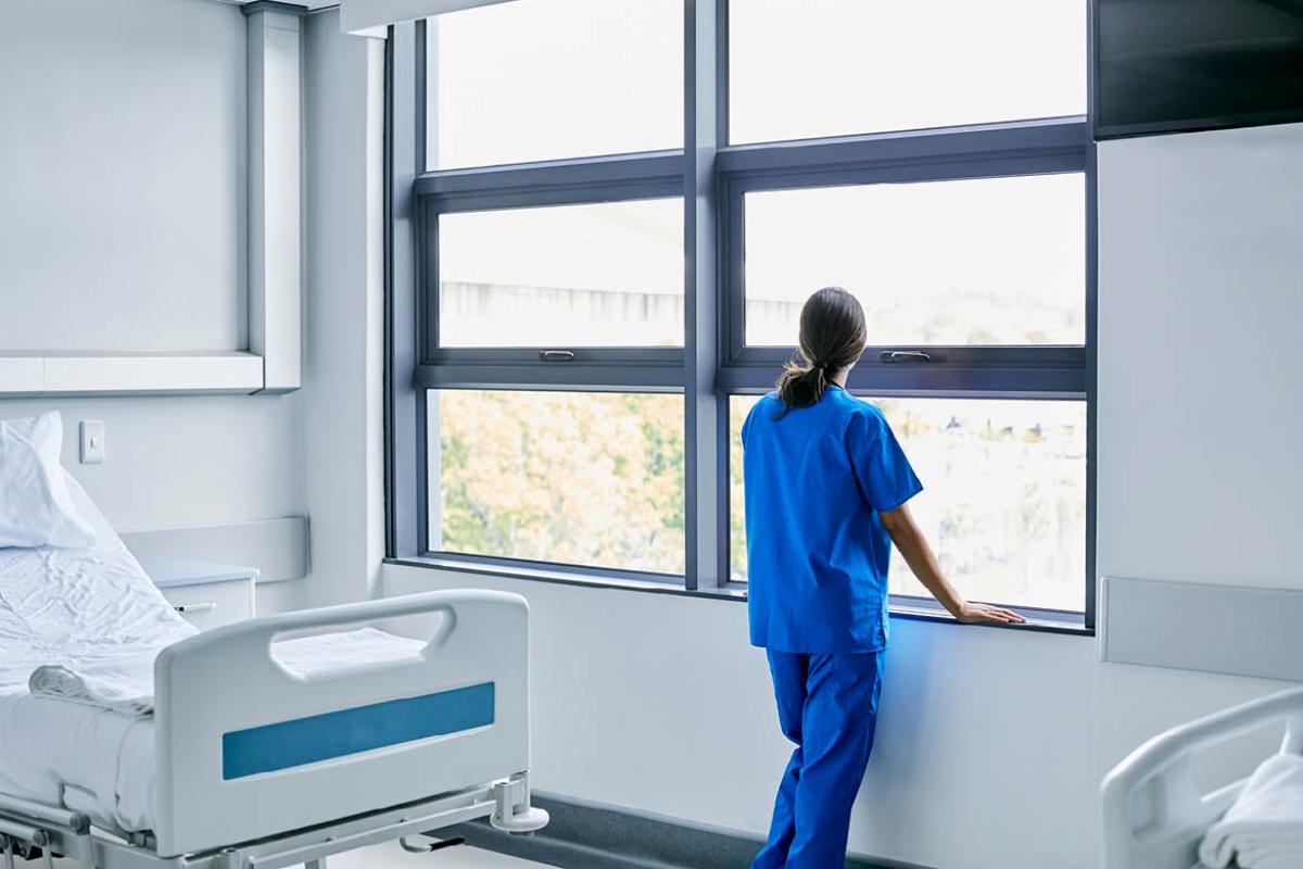 Health care worker looking out a hospital room window