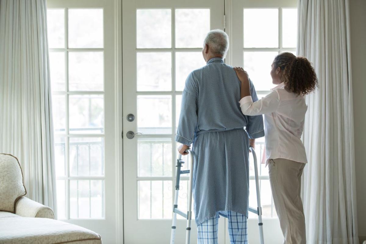 Man with walker looking out patio door with family member at his side.