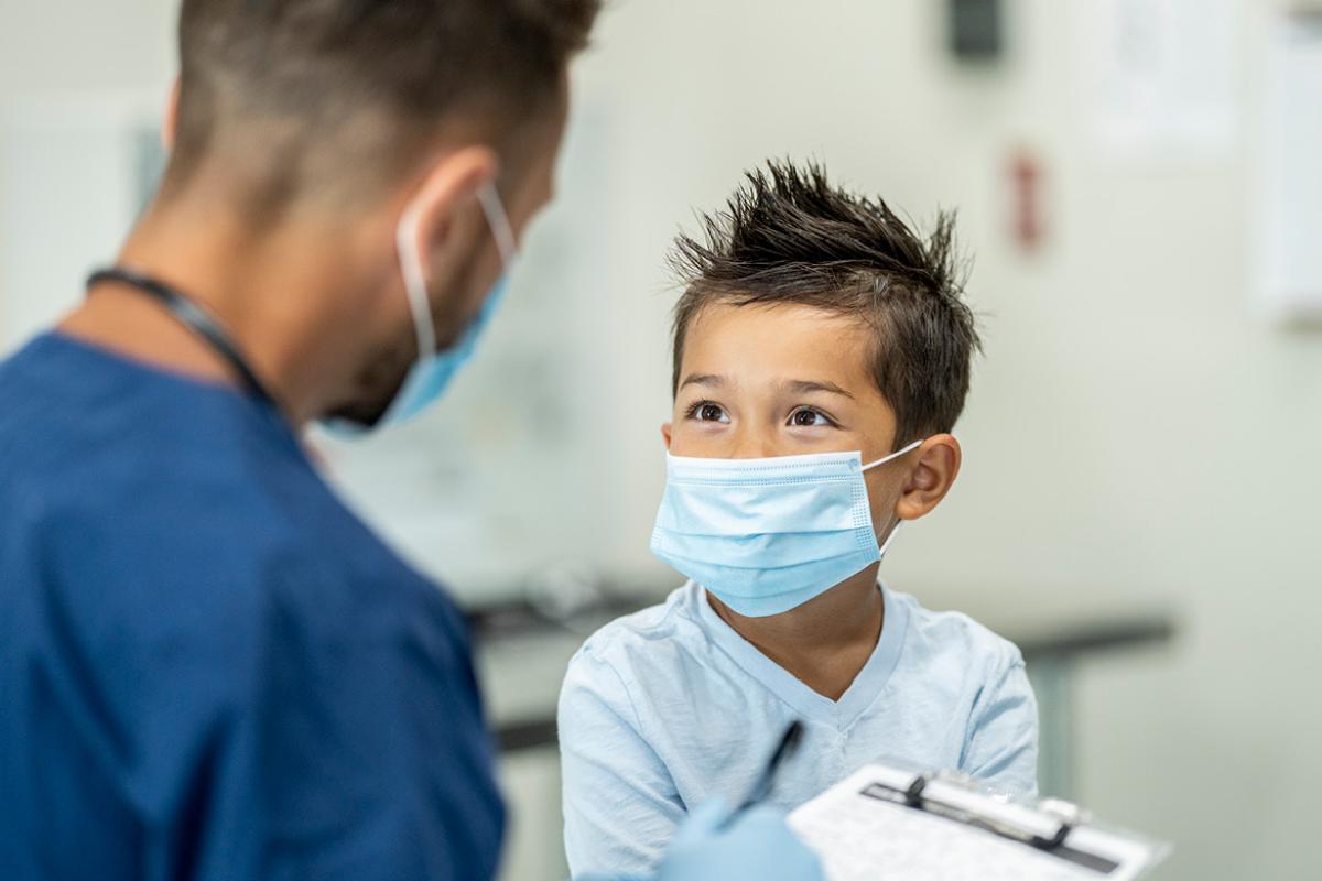 Smiling young patient wearing a mask and talking to health care worker who's taking down information.