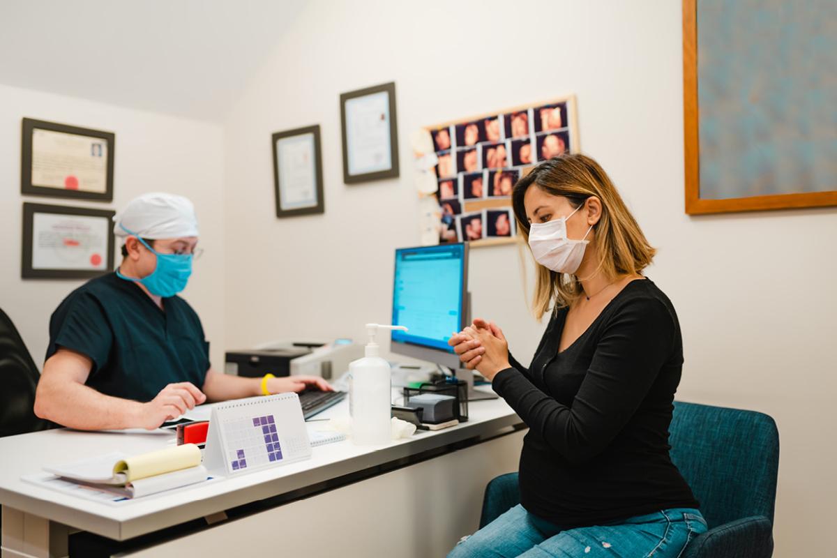 Woman waiting for doctor, both wearing masks.