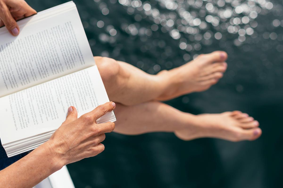 Close up of a book with the reader's legs and hands visible