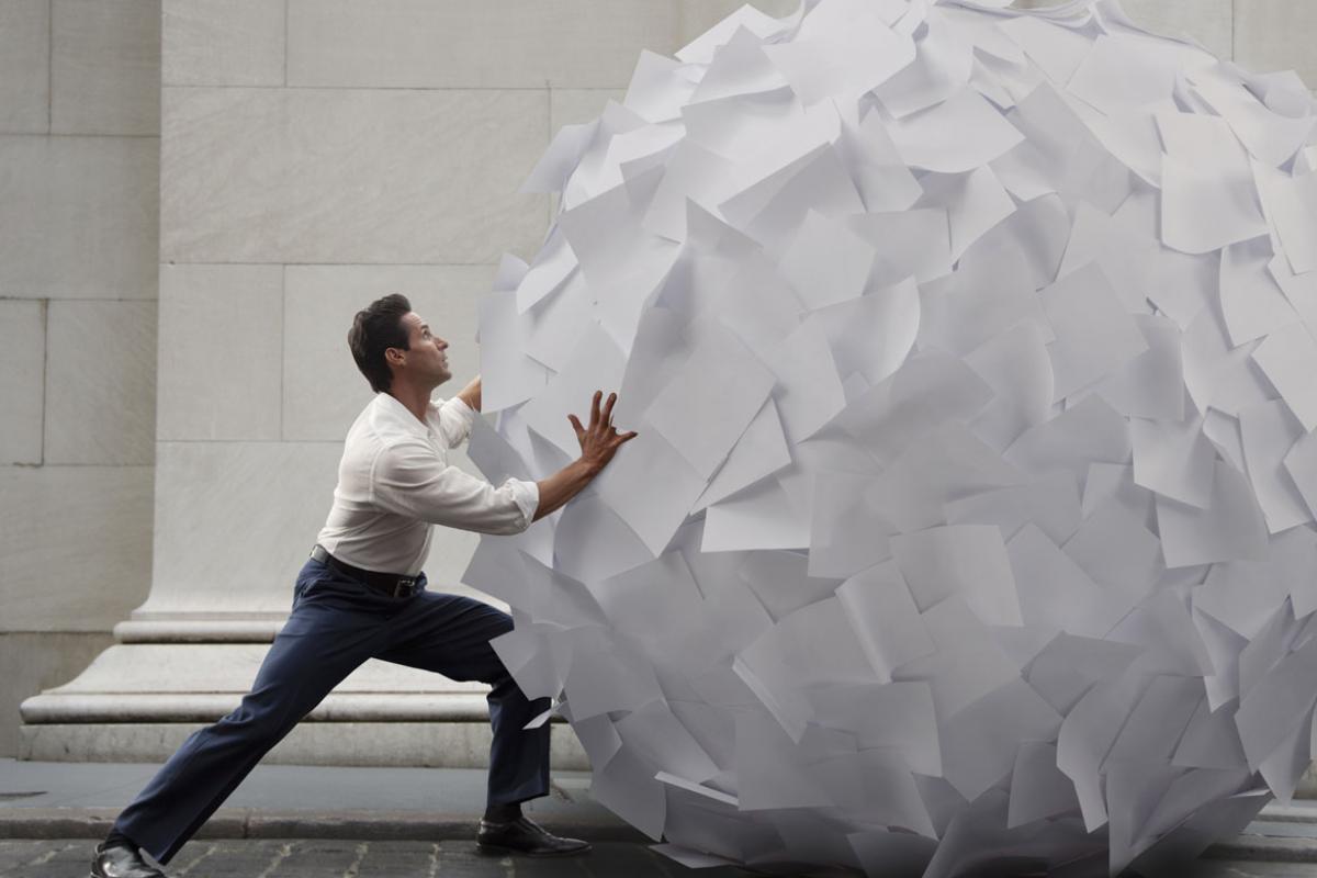 Person rolling a large ball of paper down a street