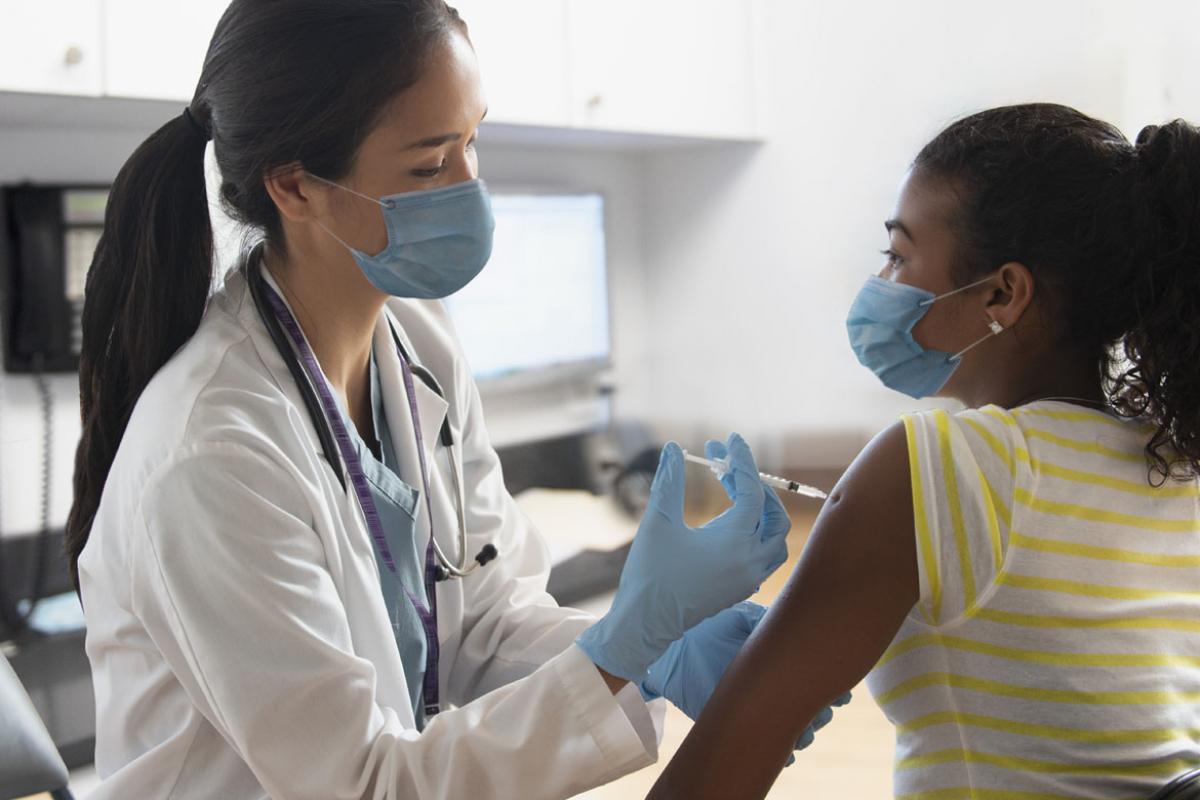 A physician giving a child a vaccination, both wearing masks.