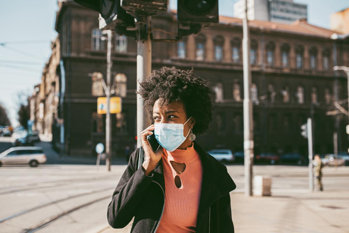 Woman walking down the street wearing a face mask and talking on a cell phone.